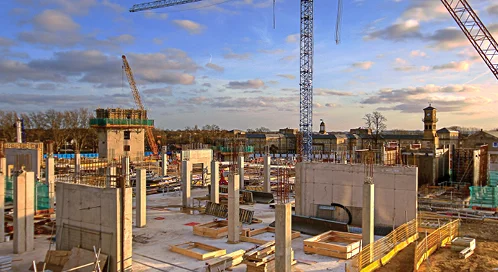 Commercial concrete building under construction with concrete columns, structural walls, and tower cranes at an active job site.