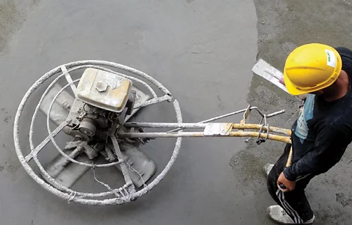 Construction worker using a power trowel to finish a freshly poured concrete slab on a commercial project.