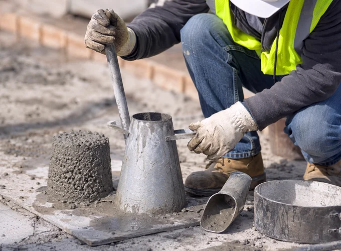 Concrete field testing technician performing a slump test with fresh concrete at a construction site.