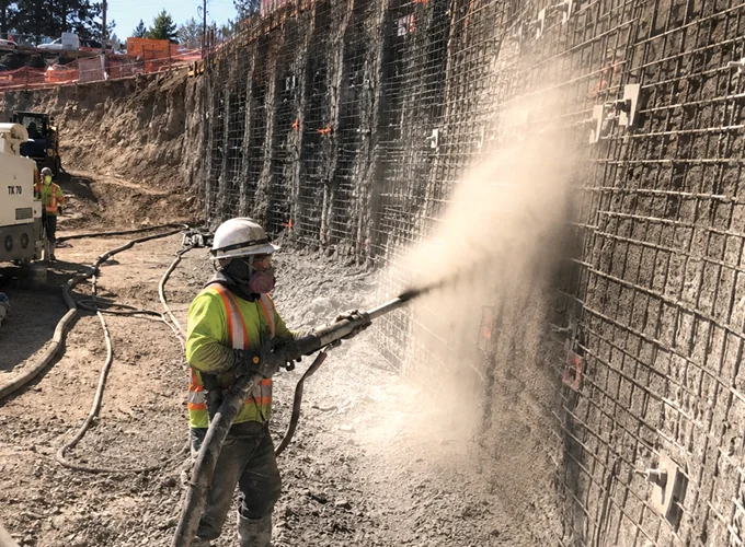 Shotcreter applying dry-mix shotcrete to a reinforced wall at a construction site.